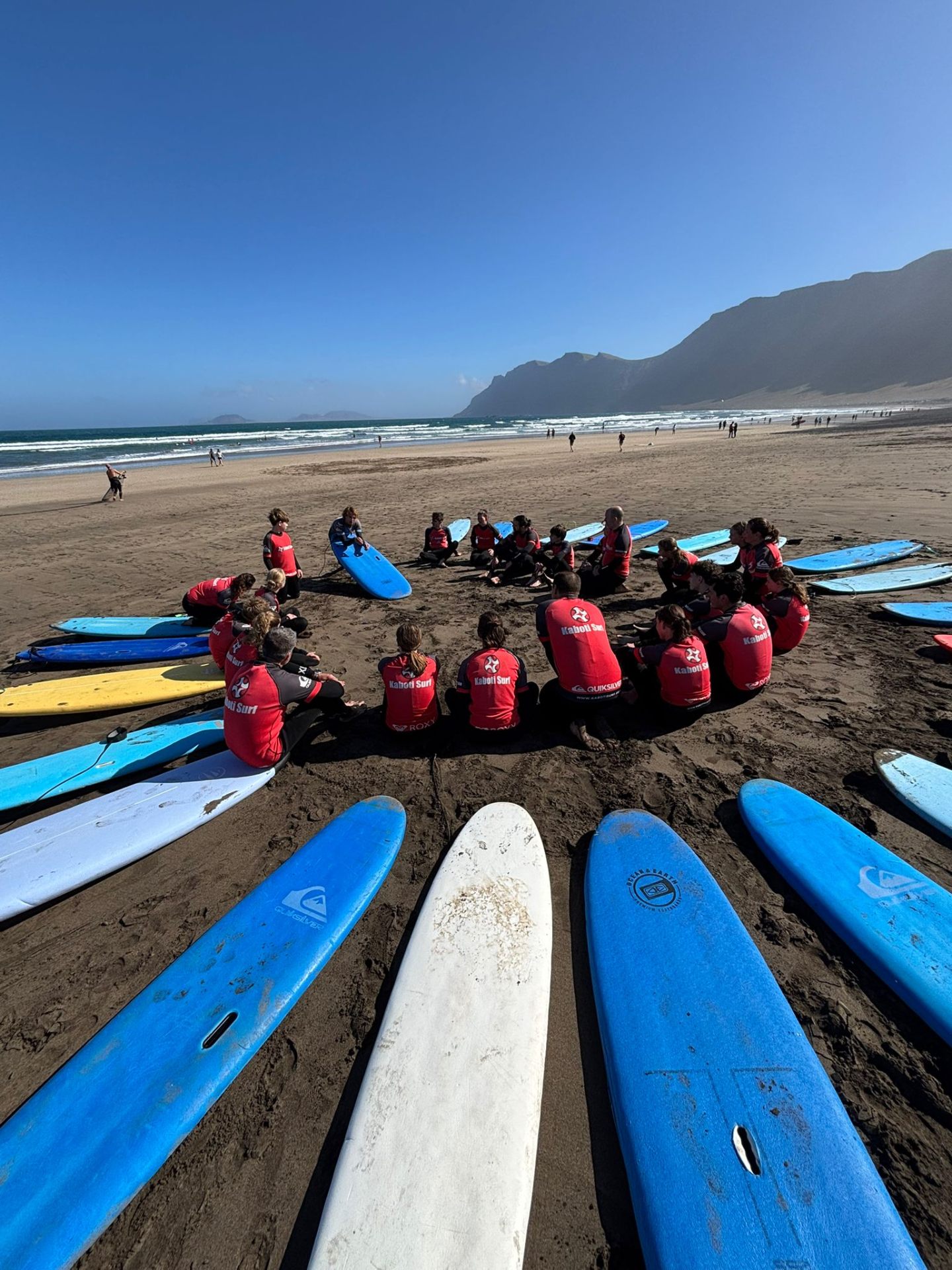 Kaboti Surf students gathered in a circle with surfboards on Famara beach